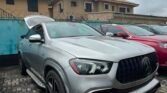 Silver luxury SUV shown from the front corner with trunk open in a paved parking lot.