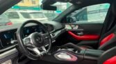 Front interior of a black and red Mercedes-Benz with a sporty steering wheel and digital dashboard.