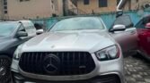 Front view of a silver Mercedes-Benz SUV parked in a lot with its driver’s door open and surrounding cars nearby, watermark on image edge.